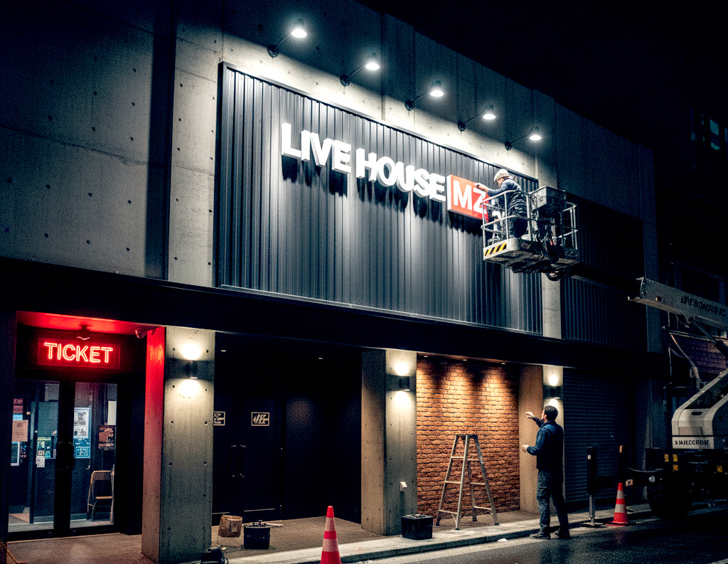 高所作業車に乗った看板職人がファサード看板のカルプ文字を取り付けている様子を写した写真