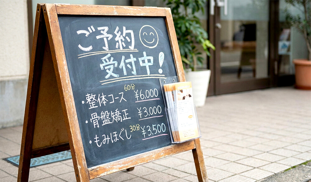 イタリアンバルの店先に置かれた黒板風のA型看板。手書きでランチメニューと価格が書かれ、写真も貼ってある